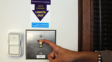 Hand turning off lights with a sign that says to conserve energy.