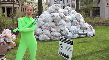Student in neon green bodysuit in front of a pile of bags of recycling