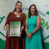 Two people, wearing dresses with long hair, holding an award at the 2022 Green Ribbon Schools ceremony