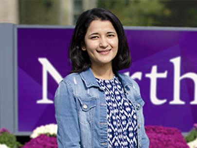 Vasundhara Agrawal standing in front of purple flowers and the Northwestern campus sign 